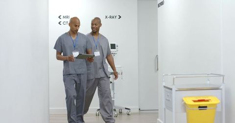 African american radiology techs walking corridor reviewing tablet in hospital imaging