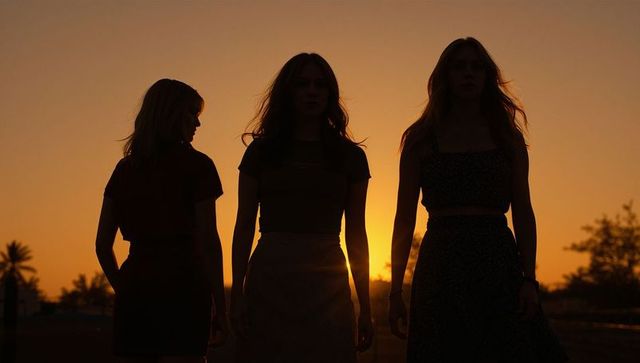 Three women walking at sunset silhouettes on road with palm trees golden hour rim-lit