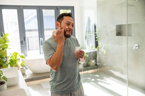 Mature asian man applying facial moisturizer in sunlit contemporary bathroom