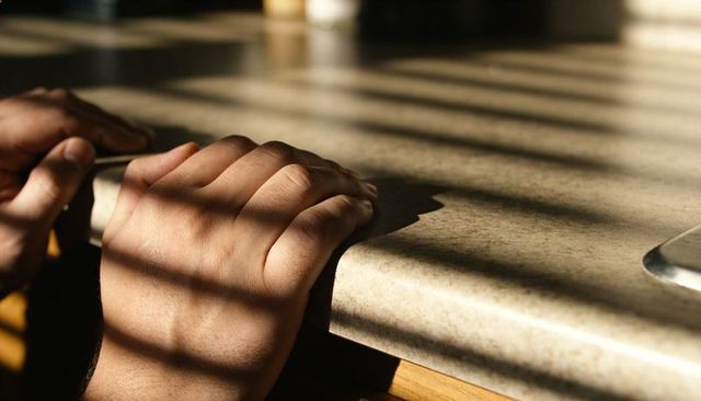 Sunlit hands gripping rounded counter edge bathed in morning light with striped blind shadows