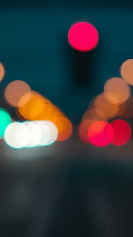 Pulsing red traffic light sending bokeh glow over night urban street vertical video