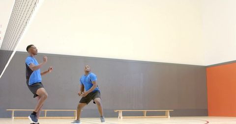 Two male athletes jumping to track volleyball on indoor gym court with dynamic motion