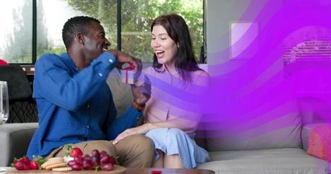 Surprising partner with gift on cozy sofa, laughing couple sharing joyful home moment