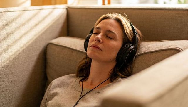 Woman reclining on sofa wearing headphones enjoying calm at-home listening and relaxation moment