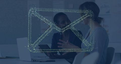 Businesswomen collaborating over devices with digital envelope overlay indicating email