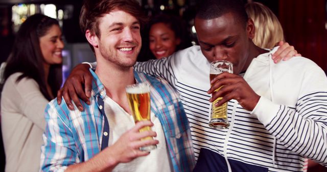 A Caucasian and an African American young man are enjoying beers together in a lively bar atmosphere, with copy space. Their cheerful demeanor and the social setting suggest a scene of friendship and relaxation.