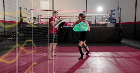 Female boxer training with coach holding curved pads in boxing ring with mirror reflection