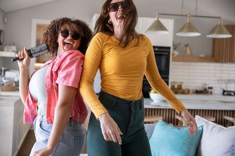 Diverse female friends singing and dancing in bright home interior