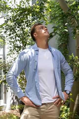 Young man standing confidently in sunlit courtyard surrounded by lush greenery