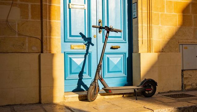 Sunlit electric scooter leaning against vibrant blue door casting dramatic shadow