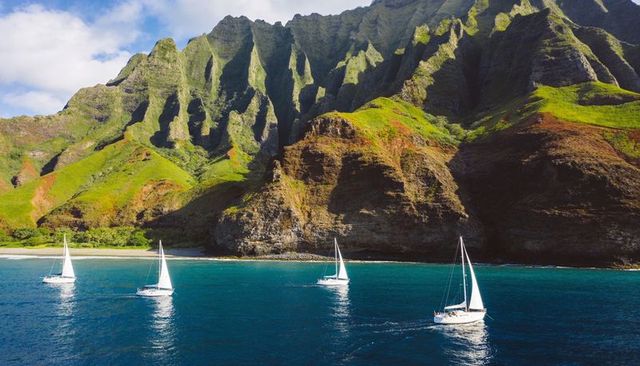 Sailboats gliding on turquoise ocean beneath towering lush cliffs for coastal escape