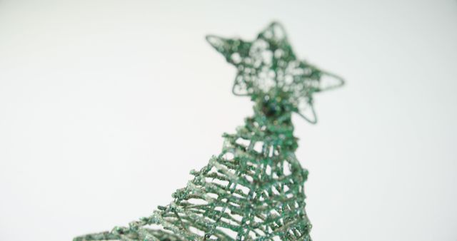 A close-up of a wireframe Christmas tree decoration with a star on top, with copy space. Its minimalist design and green hue suggest a modern take on holiday decor.