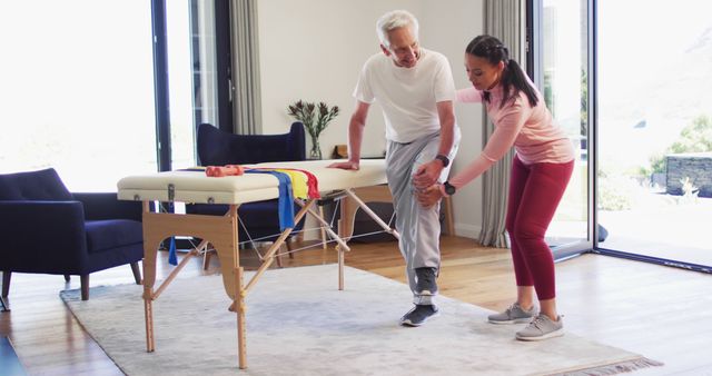 Senior man receiving help from a physical therapist during a rehabilitation session in a home environment. They are performing exercises focused on improving mobility and strength. This could be used to depict health care, elder care, physical rehabilitation, physiotherapy services, and active recovery among seniors.