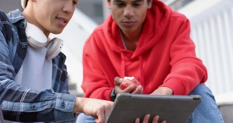 Diverse male students using tablet on campus steps studying together
