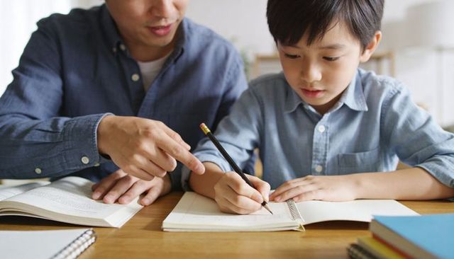 Parent guiding child writing homework at home table teaching learning together