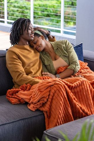 African american couple cuddling on balcony sofa under cozy orange throw, intimate moment