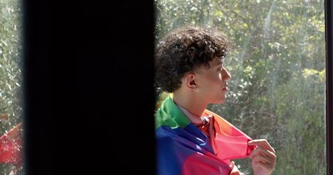 Young Man with Rainbow Flag Gazing Out Window in Peaceful Moment