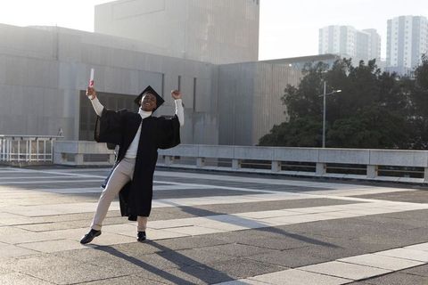 Joyful African American Graduate Celebrating on Urban Rooftop Holding Diploma Gown Cap