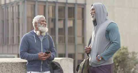 Senior African-American Men Chatting Outdoors After Workout Carrying Gym Bags and Phones