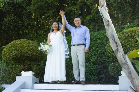 Senior asian couple celebrating wedding in lush garden, bride holding bouquet, smiling
