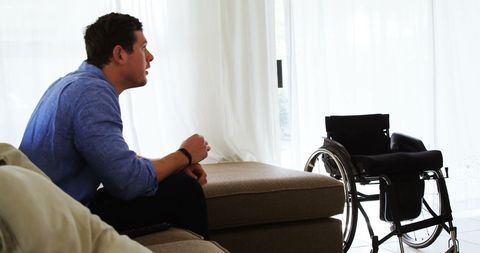 Disabled man contemplating next to wheelchair in living room