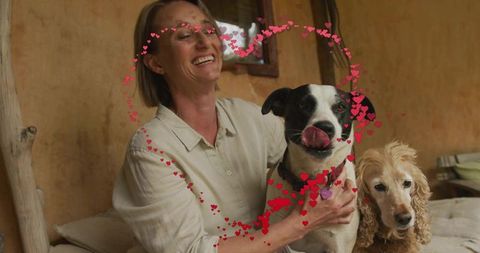 Smiling woman holding two dogs on sofa with heart overlay, cozy homely companionship