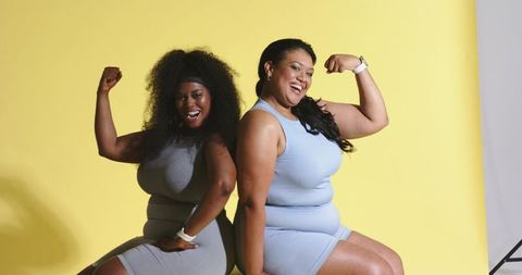 Plus size diverse women flexing in athleisure back-to-back on yellow backdrop