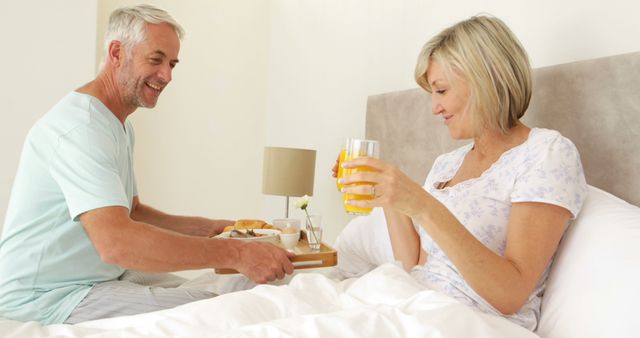 Romantic husband bringing his smiling wife breakfast in bed at home in bedroom