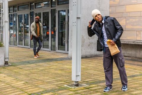Young men calling on smartphone while walking through urban plaza holding takeout bag