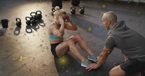 Female athlete doing sit-ups while coach holding feet in functional gym training session