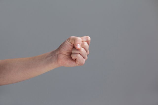 This image shows a close-up of a clenched fist against a grey background, symbolizing strength, determination, and defiance. It can be used in contexts related to empowerment, protest, solidarity, and emotional expression. Ideal for articles, campaigns, and social media posts focusing on human rights, activism, and personal strength.