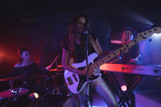 Group of confident females performing live music on an illuminated stage in a nightclub. Ideal for use in articles or promotions related to live music events, nightlife, female musicians, and entertainment industry.