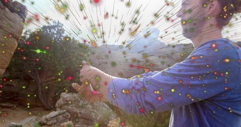Man holding device on canyon outcrop with colorful radial particle overlay, tech fusion