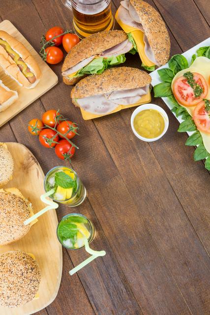 Salad, hot dogs, burgers and two glasses of mojito on wooden board