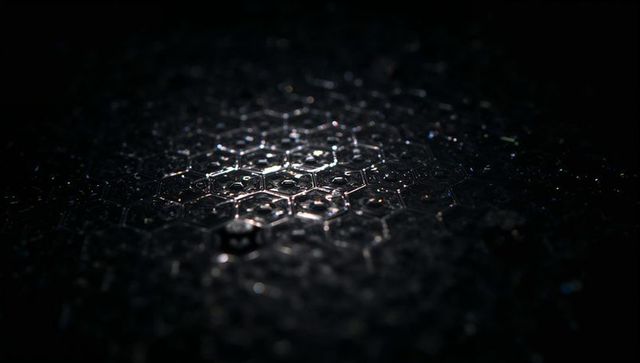 Hexagonal honeycomb surface shining with water droplets in dark macro closeup