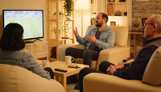 Friends watching soccer match with man gesturing and chatting in cozy warm living room