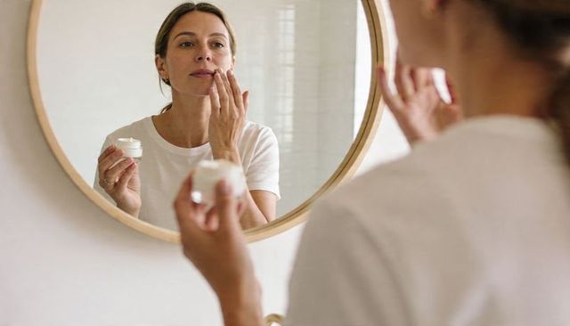 Woman applying facial moisturizer in round mirror morning skincare selfcare routine