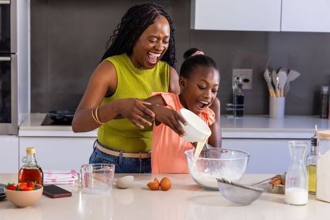 Mother and daughter joyfully baking together in modern kitchen pouring batter and smiling