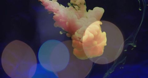 Billowing peach ink plume floating in water with blue bokeh and green filaments