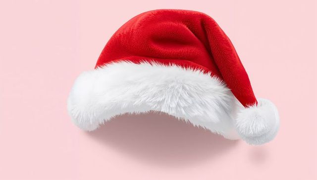 Red velvet santa hat on pastel pink background with white fur trim and pompom