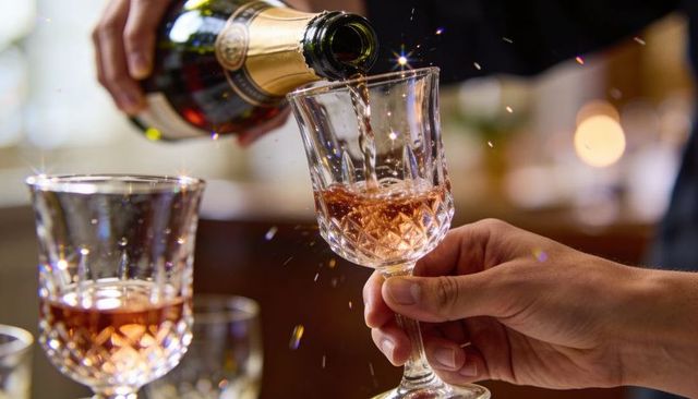 Pouring sparkling rosé into cut crystal goblet from gold-foil bottle with bokeh sparkle