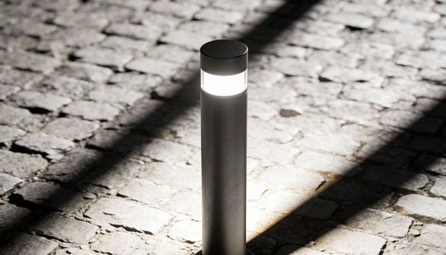 Modern bollard light illuminating cobblestone plaza with dramatic diagonal shadows