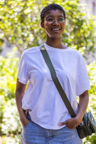 Smiling african woman wearing white tee and denim with glasses and crossbody bag in sunlit park