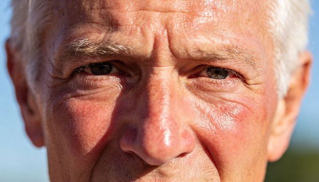 Squinting senior man in sunlight revealing wrinkles and natural skin texture outdoor portrait