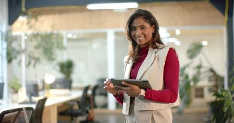 Indian Businesswoman Holding Tablet and Smiling in Modern Open-Plan Office Workspace