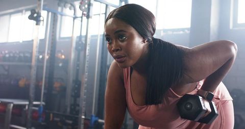 African american woman performing dumbbell row on bench, sweating, focused strength training