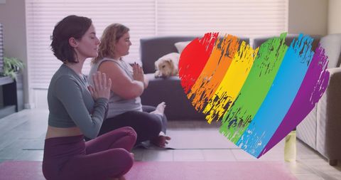 Lesbian couple doing yoga at home with rainbow heart symbol