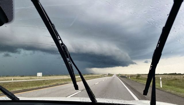 Windshield view of dark shelf cloud looming over rural highway with wipers clearing rain