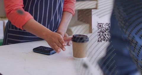 Barista placing takeaway coffee beside contactless payment terminal on marble counter