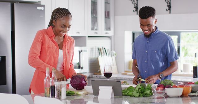 Young couple enjoying quality time preparing meal, following a recipe on tablet. Ideal for topics on healthy eating, using technology for cooking, modern lifestyle, and culinary activities for couples.